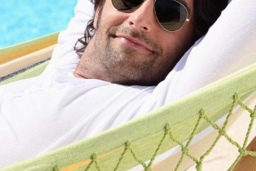 man in hammock wearing sunglasses by swimming pool