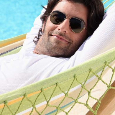 man in hammock wearing sunglasses by swimming pool