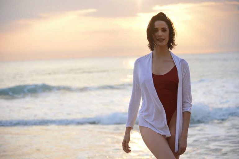 beautiful woman in a deep red one piece swimsuit wearing a white loose cover-up shirt