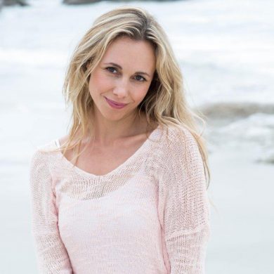 Blonde at beach wearing a pink thin sweater cover-up